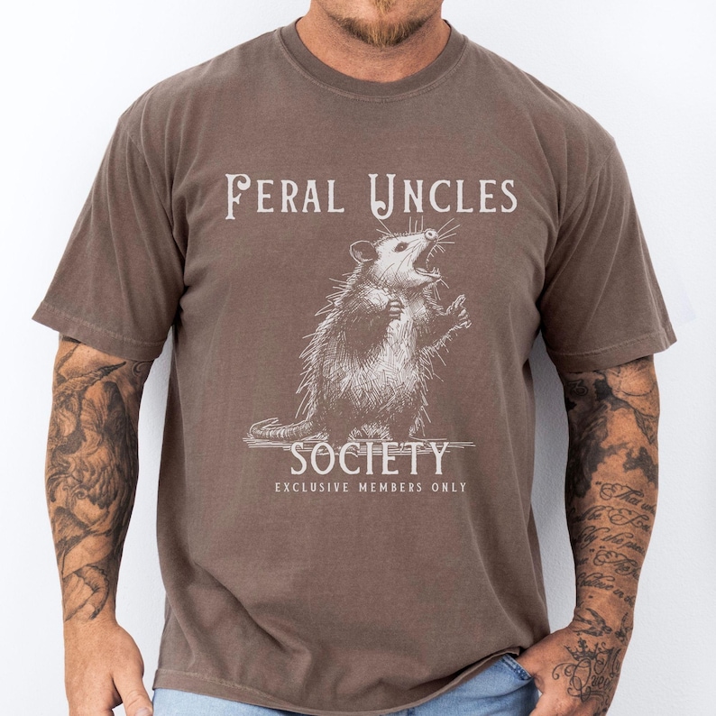 May include: A brown t-shirt with a white graphic of a possum and the text "Feral Uncles Society Exclusive Members Only".