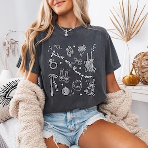 Puede incluir: Camiseta gris oscuro con ilustraciones en blanco de elementos relacionados con bodas, como un anillo, zapatos, copas de champ&aacute;n y un pastel en forma de coraz&oacute;n. El texto "future mrs. Thompson" tambi&eacute;n est&aacute; en la camiseta.