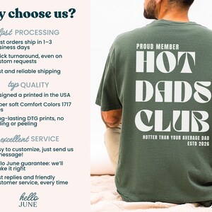 May include: A dark green t-shirt with the text "HOT DADS CLUB" in large white letters on the back. The shirt also includes the phrases "PROUD MEMBER" and "HOTTER THAN YOUR AVERAGE DAD ESTD 2026".