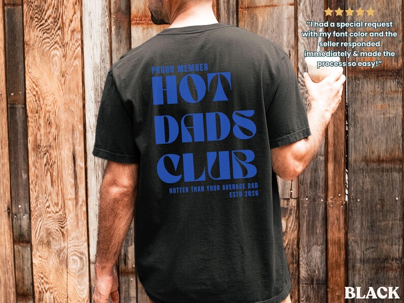 May include: Black t-shirt with the text "HOT DADS CLUB" in blue, with "PROUD MEMBER" above and "HOTTER THAN YOUR AVERAGE DAD ESTD 2026" below. The shirt is a casual style.