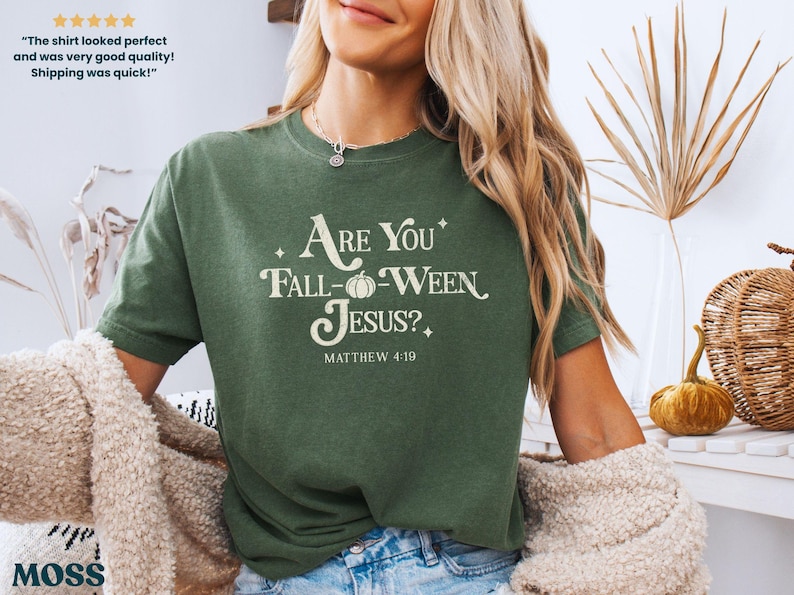 May include: Green t-shirt with the text "Are You Fall-Ween Jesus?" and "Matthew 4:19" in white. The shirt has a relaxed fit and is made of a soft material. The design includes a pumpkin graphic. The shirt is part of a fall-themed collection.