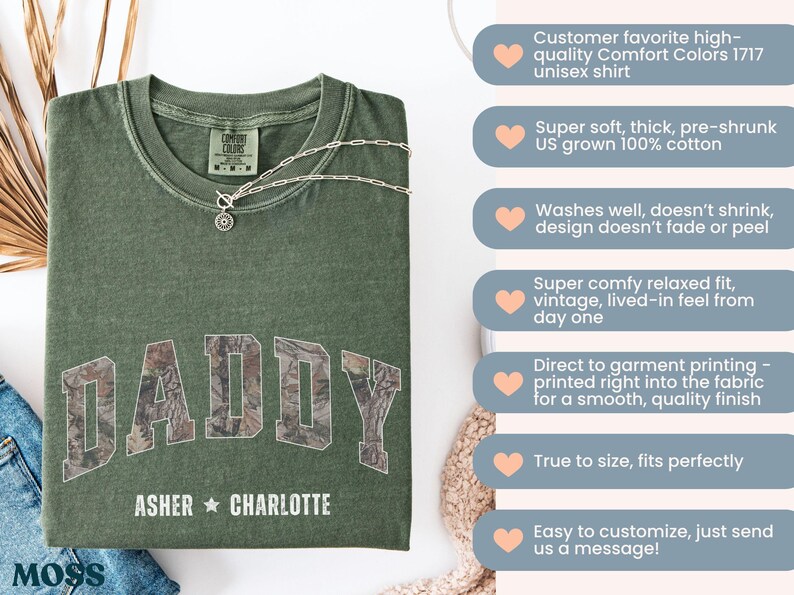 K&ouml;nnte beinhalten: Ein olivgr&uuml;nes Unisex-T-Shirt mit dem Wort "DADDY" in einem Camouflage-Muster auf der Brust. Darunter stehen die Namen "ASHER" und "CHARLOTTE". Eine silberne Halskette mit Anh&auml;nger liegt auf dem Shirt.
