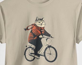 May include: A beige t-shirt with a graphic of a cat wearing a red scarf and riding a bicycle.