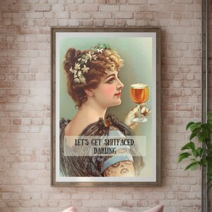 May include: A vintage-style print with a woman holding a glass of beer. The print has a light blue background and the text "Let's get shitfaced, darling".