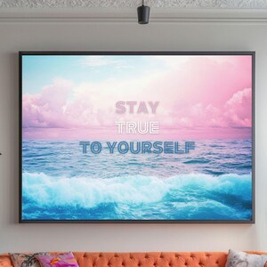 Peut inclure: Un intérieur de salon avec un canapé orange clair, un pouf bleu et une impression encadrée avec le texte "STAY TRUE TO YOURSELF" sur fond de ciel rose et bleu et de vagues océaniques.