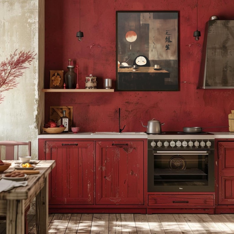 May include: A rustic kitchen with red cabinets and walls. A framed artwork with a Japanese theme hangs above the sink. A stainless steel kettle sits on the stovetop. The kitchen has a wooden table and a shelf with decorative items.