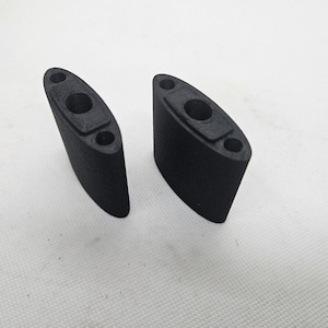 May include: Two black, oval-shaped components with a textured surface. Each has a central hole and two smaller holes. The objects are positioned on a white surface, suggesting a product shot for an industrial or mechanical part.