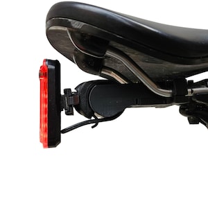 Könnte beinhalten: Ein schwarzer Fahrradsattel mit einem roten LED-Rücklicht. Das Licht ist rechteckig und hat eine Reihe roter LEDs. Der Sattel ist schwarz und hat ein geschwungenes Design. Das Licht ist an einer schwarzen Halterung befestigt.