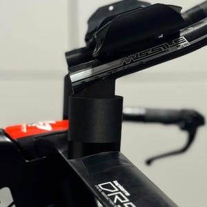 Peut inclure: Gros plan sur un guidon de vélo noir avec le texte "DRS" et "MISSILE" en blanc. Le guidon a un design aérodynamique élégant, avec un repose-bras rembourré noir. Le cadre du vélo est noir et rouge.