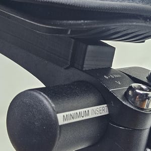 Peut inclure: Gros plan sur un composant noir de vélo avec une chaussure posée dessus. Le composant porte une étiquette indiquant "MINIMUM INSERT" et une jauge de 6-8 Nm. L'image est bien éclairée, mettant en valeur les textures et les détails des pièces.