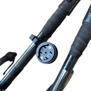 May include: Close-up of a black bicycle handlebar with a black grip and a round black device attached. The device has a circular design with a central mounting point and two small screws. The handlebar has the text "DURA-ACE".