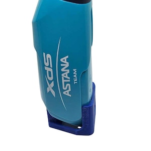 Pode incluir: Uma garrafa de água turquesa brilhante com tampa azul-escura e suporte de base azul. A lateral da garrafa exibe o texto branco XDS ASTANA TEAM com um gráfico de linha curva. A garrafa tem uma construção de plástico lisa e contornada.