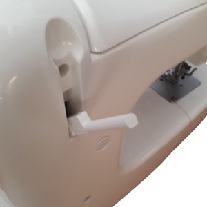 Peut inclure: Gros plan sur une machine à coudre blanche. La machine est dotée d'un levier blanc et d'une plaque à aiguille. Le corps de la machine est blanc brillant. L'image est bien éclairée, mettant en valeur les détails de la machine.