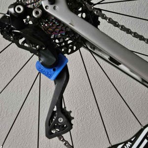 Peut inclure: Gros plan sur la roue arrière et la transmission d'un vélo. L'image met en évidence le dérailleur noir, la chaîne et la cassette contre un cadre argenté. Un composant bleu avec le texte "csc3d" est visible. La jante de la roue a un design noir et blanc.