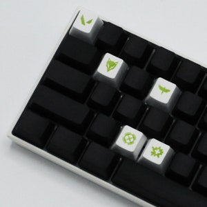 May include: A black keyboard with white keycaps featuring green symbols. The symbols include a fox, a butterfly, a gear, and a circle with a cross inside.