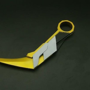 May include: A gold and black stylised knife with a curved blade and a ring handle.
