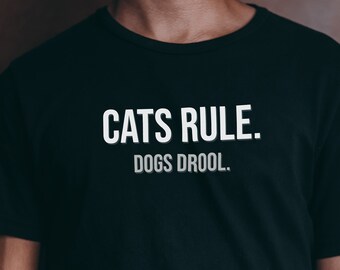 Może przedstawiać: Czarny T-shirt z białym napisem "CATS RULE. DOGS DROOL."