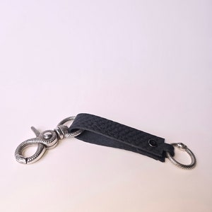 May include: A black leather key chain with a silver snake-shaped hook and a silver ring.