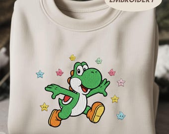 May include: A cream-colored sweatshirt featuring an embroidered Yoshi character in green, white, and orange, with colorful star accents. The word "EMBROIDERY" is printed on the top right corner of the sweatshirt.
