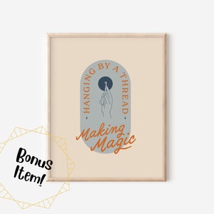 Könnte beinhalten: Ein gerahmter Kunstdruck mit beigem Hintergrund. Das Kunstwerk zeigt ein bogenförmiges Design mit den Worten "Hanging by a Thread" und "Making Magic". Eine Hand wird dargestellt, die einen Faden hält. Der Rahmen ist hellbraun.