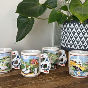 May include: Set of five white ceramic mugs with goose handles. Each mug features a different colorful illustration of geese and a countryside scene.