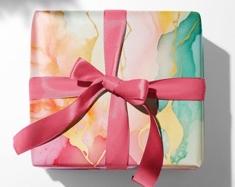 May include: A gift box wrapped in colorful abstract paper with pink, yellow, and green watercolor-like swirls. A bright pink satin ribbon is tied in a bow on top of the box.