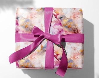 May include: A gift box wrapped in white paper with a watercolor design of birds and flowers. The box is tied with a bright pink ribbon.
