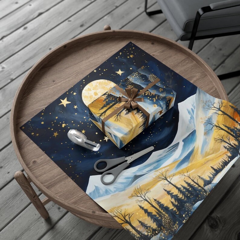 May include: A gift wrapped in blue and gold wrapping paper with a mountain and forest scene. The paper features a full moon, stars, and gold glitter. The gift is tied with a brown ribbon.