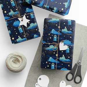 May include: Three gift boxes wrapped in blue and gold wrapping paper with a starry night sky and blue police boxes pattern. The boxes are tied with twine and decorated with white paper stars and hearts.