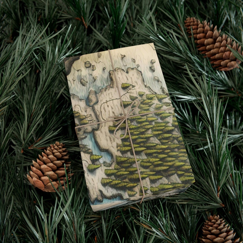 Puede incluir: Una caja de regalo envuelta con un dise&ntilde;o de mapa dibujado a mano que presenta una escena de bosque en tonos de verde y marr&oacute;n. La caja est&aacute; atada con cuerda y se encuentra sobre un lecho de agujas de pino verdes.