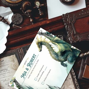 K&ouml;nnte beinhalten: Eine Hochzeit RSVP-Karte mit einer Illustration eines gr&uuml;nen und goldenen Drachen. Die Karte hat einen wei&szlig;en Hintergrund und den Text "RSVP MIA & ROBERT Bitte antworten Sie bis zum 12. Oktober 2025 Akzeptiert mit Vergn&uuml;gen Anzahl der Teilnehmer Lehnt mit Bedauern ab".