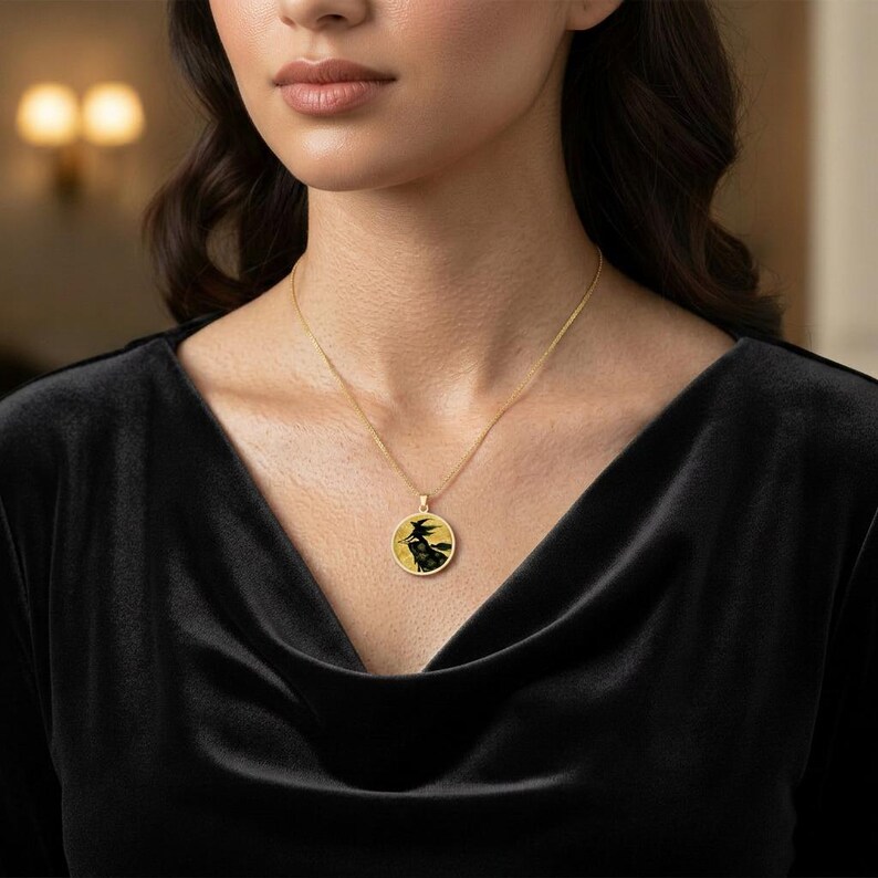 May include: A gold chain necklace featuring a round pendant with a black silhouette of a witch flying on a broomstick against a yellow background. The pendant is circular with a gold border and hangs from a delicate gold link chain.