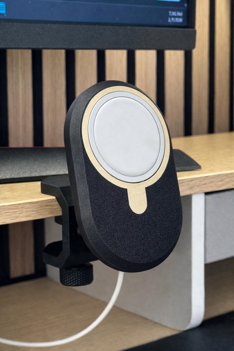 K&ouml;nnte beinhalten: Eine schwarz-goldene magnetische Ladestation mit einer kreisf&ouml;rmigen wei&szlig;en Mitte, die eine strukturierte Oberfl&auml;che und einen stabilen Klemmmechanismus mit einem ger&auml;ndelten Einstellknopf aufweist, um sicher an einer Tischkante zu befestigen.