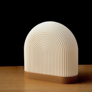 May include: A white ceramic lamp with a rounded arch shape and a brown base. The lamp has a textured surface with horizontal lines.