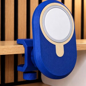 K&ouml;nnte beinhalten: Eine blaue magnetische Ladestation mit einer kreisf&ouml;rmigen wei&szlig;en Mitte und einem goldfarbenen Akzentring. Das Ger&auml;t verf&uuml;gt &uuml;ber einen C-Klemmen-Mechanismus mit einem strukturierten blauen Einstellknopf zur sicheren Befestigung an einer Kante.
