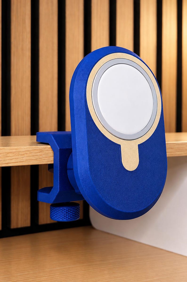 K&ouml;nnte beinhalten: Eine blaue magnetische Ladestation mit einer kreisf&ouml;rmigen wei&szlig;en Mitte und einem goldfarbenen Akzentring. Das Ger&auml;t verf&uuml;gt &uuml;ber einen C-Klemmen-Mechanismus mit einem strukturierten blauen Einstellknopf zur sicheren Befestigung an einer Kante.