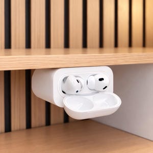May include: White wireless earbuds in a charging case, partially open. The case is mounted under a wooden shelf. The background features vertical wooden slats and a wooden surface. The earbuds are a modern tech accessory.