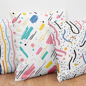 May include: Three decorative throw pillows with abstract patterns in black, white, pink, yellow, blue, and orange. The patterns include stripes, dots, and squiggly lines.