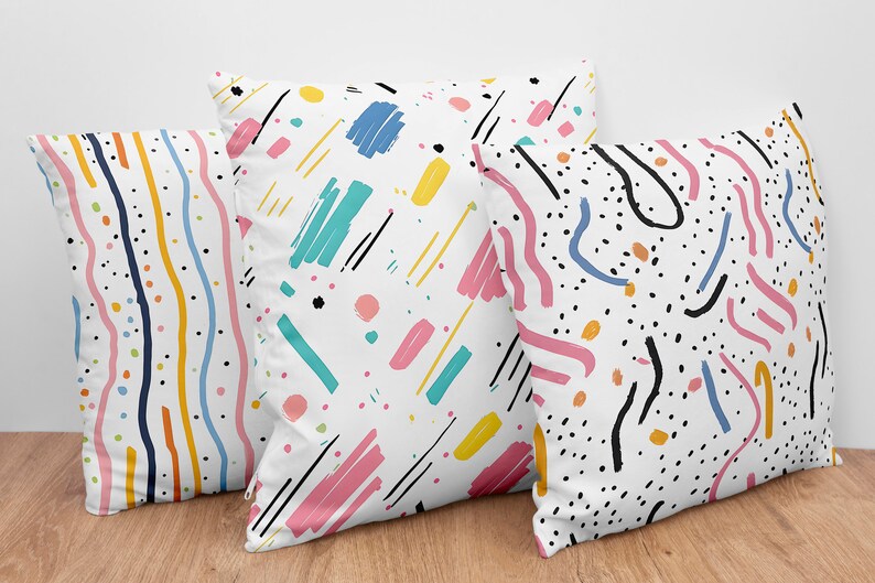 May include: Three decorative throw pillows with abstract patterns in black, white, pink, yellow, blue, and orange. The patterns include stripes, dots, and squiggly lines.
