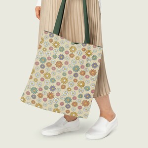 Pode incluir: Uma pessoa est&aacute; carregando uma bolsa tote grande com um padr&atilde;o floral. A bolsa &eacute; feita de lona e tem uma al&ccedil;a verde. O padr&atilde;o &eacute; um desenho repetitivo de pequenas margaridas em v&aacute;rios tons de amarelo, laranja, rosa e verde.