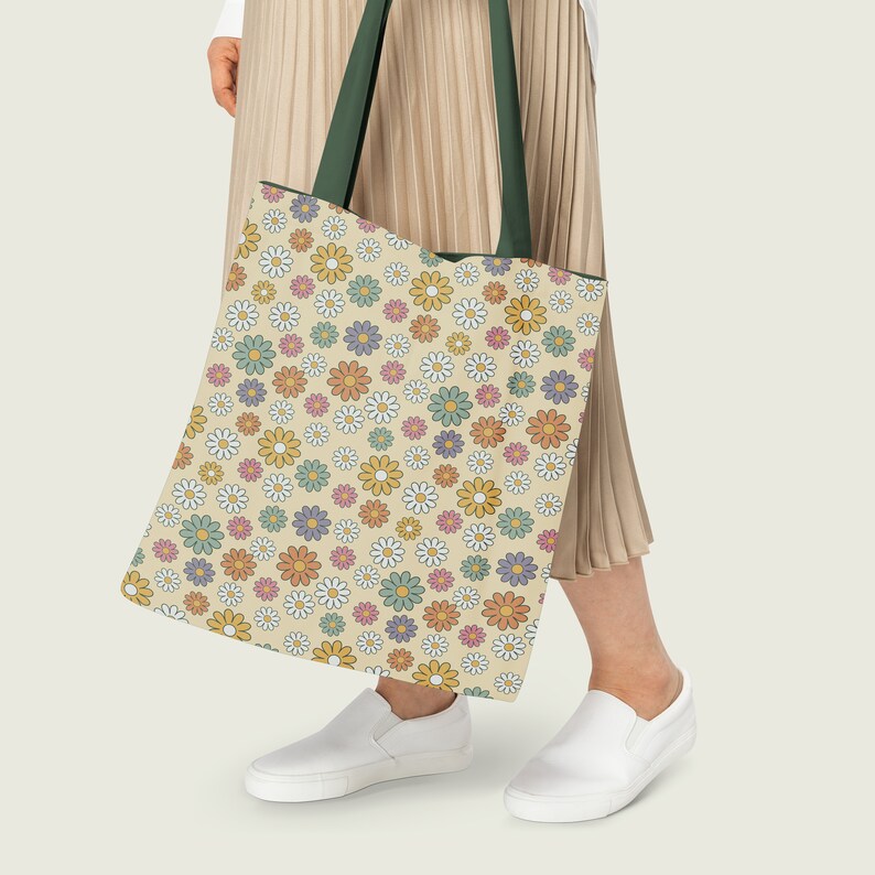 Pode incluir: Uma pessoa est&aacute; carregando uma bolsa tote grande com um padr&atilde;o floral. A bolsa &eacute; feita de lona e tem uma al&ccedil;a verde. O padr&atilde;o &eacute; um desenho repetitivo de pequenas margaridas em v&aacute;rios tons de amarelo, laranja, rosa e verde.