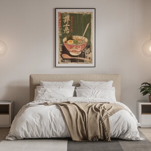 May include: A white bed with a tan blanket and two white pillows. A framed poster of a bowl of ramen with Japanese characters hangs above the bed.