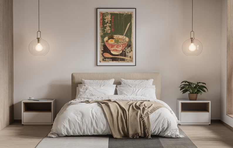 May include: A white bed with a tan blanket and two white pillows. A framed poster of a bowl of ramen with Japanese characters hangs above the bed.