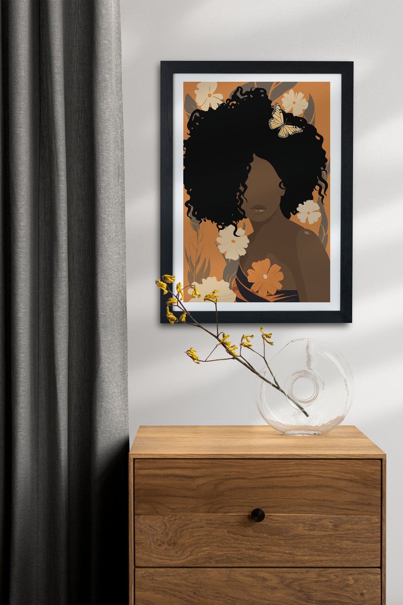 Pu&ograve; includere: Un'illustrazione incorniciata di una donna con la pelle marrone scuro e capelli neri ricci. Indossa un vestito a fantasia e ha una farfalla sui capelli. Lo sfondo &egrave; di colore arancione caldo con fiori gialli.