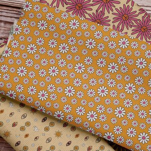 Pode incluir: Tr&ecirc;s amostras de tecido com padr&otilde;es diferentes. A amostra superior tem um padr&atilde;o floral rosa e branco. A amostra do meio tem um fundo amarelo com margaridas brancas. A amostra inferior tem um fundo amarelo com um padr&atilde;o repetitivo de olhos, s&oacute;is e luas.