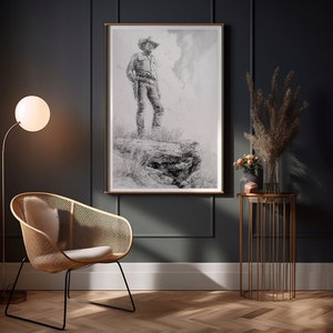 May include: A black and white drawing of a cowboy standing on a rock, framed in a gold frame and hanging on a dark gray wall. A wicker chair with a white cushion sits in front of the artwork, and a gold metal side table with a vase of dried flowers sits to the right.