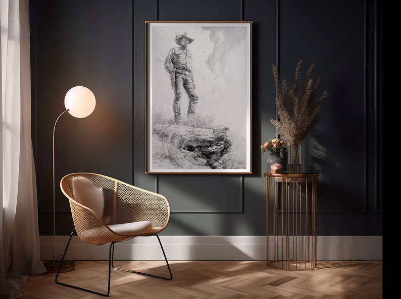 May include: A black and white drawing of a cowboy standing on a rock, framed in a gold frame and hanging on a dark gray wall. A wicker chair with a white cushion sits in front of the artwork, and a gold metal side table with a vase of dried flowers sits to the right.