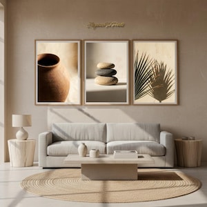 Può includere: Tre stampe artistiche incorniciate con un vaso di terracotta, pietre impilate e l'ombra di una foglia di palma. Le stampe sono sopra un divano grigio chiaro, con un tappeto beige e tavolini in legno. La stanza ha una palette di colori neutri.