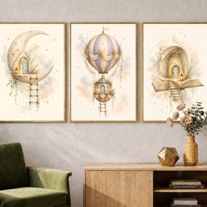 Può includere: Un set di tre stampe artistiche da parete incorniciate con illustrazioni ad acquerello. La prima mostra una luna crescente con porta e scala, la seconda una mongolfiera con casa, e la terza un libro aperto con porta e una scalinata.