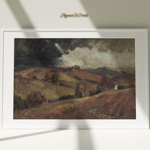 Può includere: Un dipinto di paesaggio incorniciato raffigura colline ondulate sotto un cielo drammatico. L'opera presenta una tavolozza di colori tenui di marroni, verdi e grigi, con un piccolo edificio visibile su una collina lontana. La cornice è bianca.
